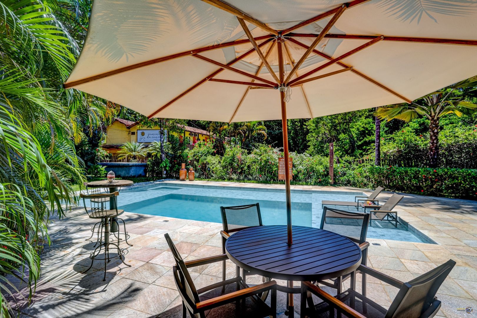 Uma mesa e cadeiras sob um guarda-sol ao lado de uma piscina.