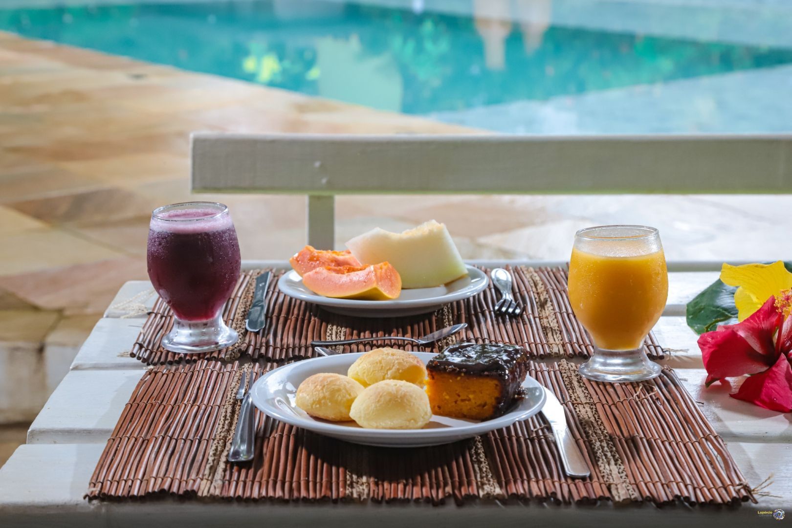 Uma mesa com pratos de comida e bebidas em frente a uma piscina.
