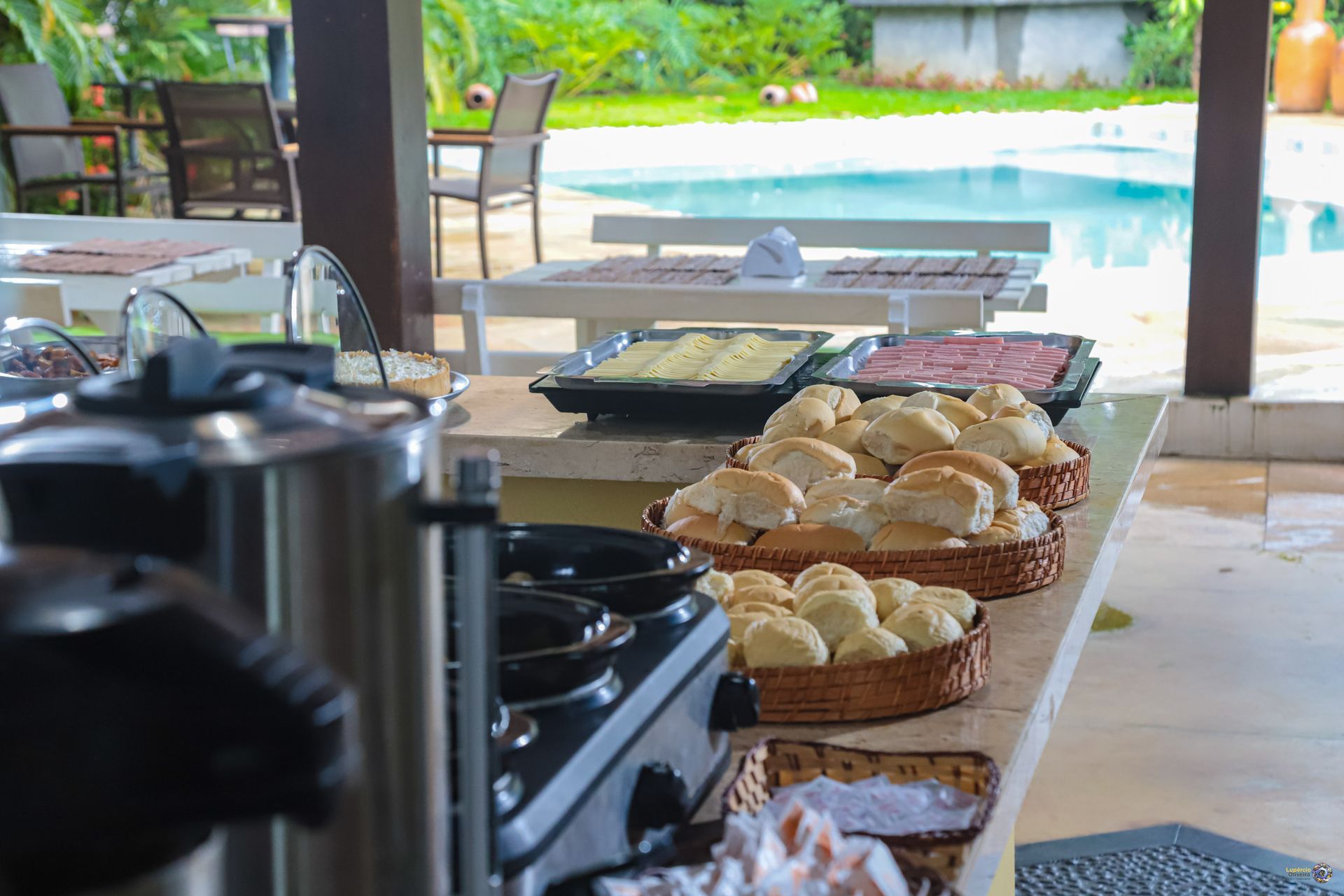 Uma mesa com pratos de comida e bebidas com uma piscina ao fundo.