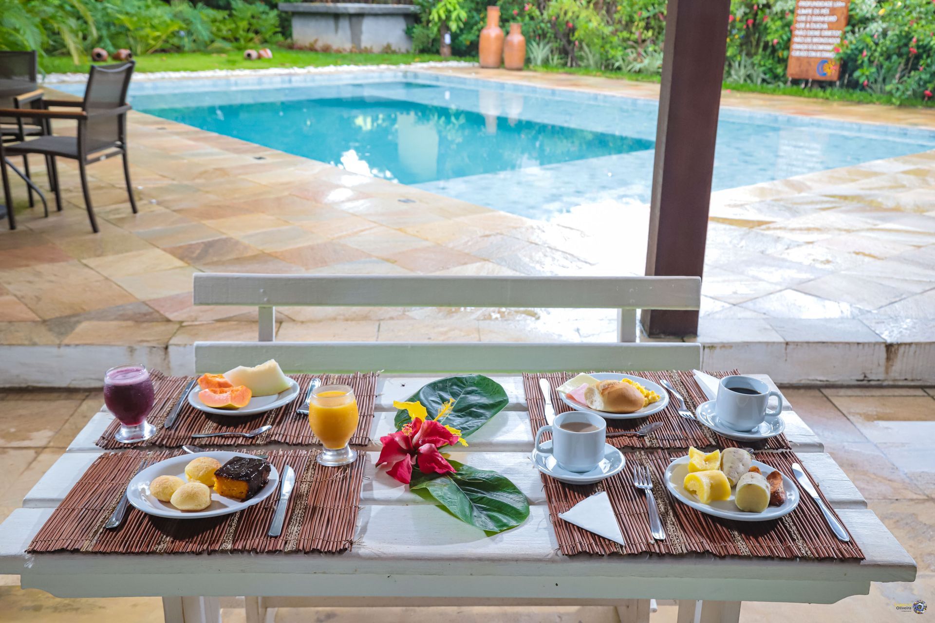 Uma mesa com pratos de comida e bebidas em frente a uma piscina.