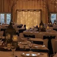Elegant candlelit restaurant dining room with set tables, white chair covers, and sheer drapes.