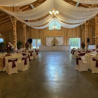 Elegant banquet hall with draped ceiling, white chairs with burgundy bows, and a lit head table at the far end