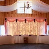 Elegant wedding reception backdrop with white drapes, pink fabric, and string lights behind a decorated table