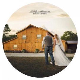 Bride and groom walking toward a yellow barn at sunset, with a circular vignette and watermark text