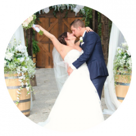 Bride and groom kissing beneath white floral arches at a wedding ceremony