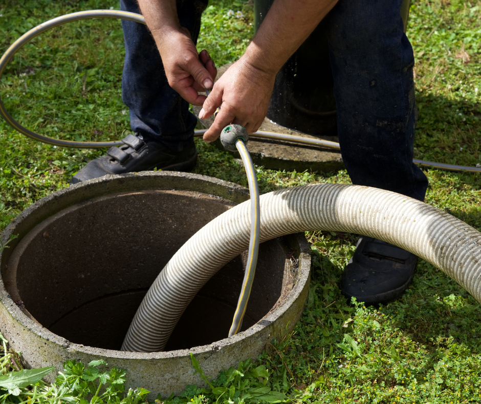 Man inserting a hose into an open septic tank in a grassy yard.