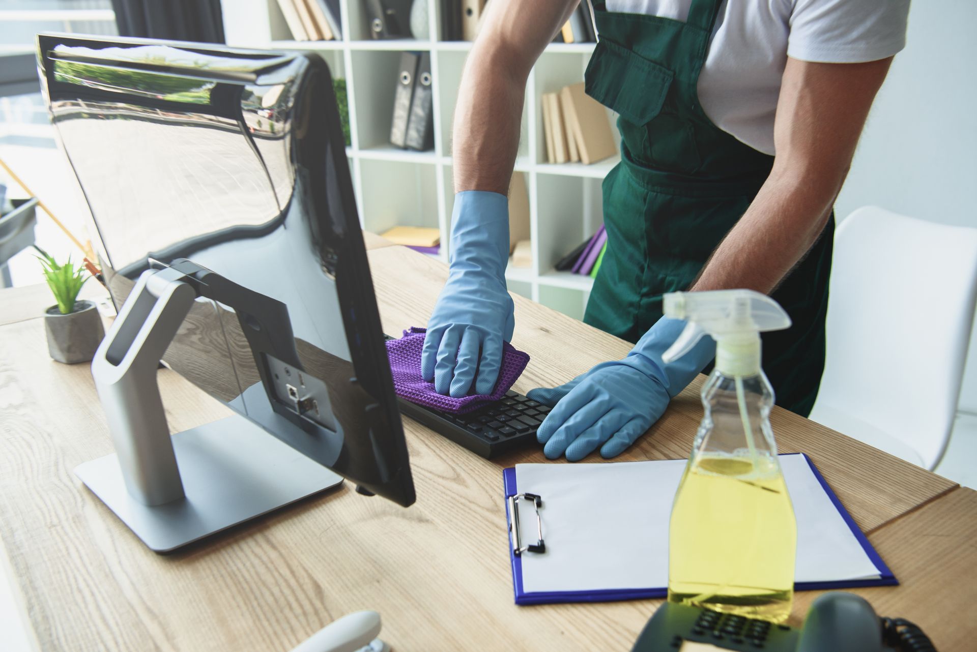 Professional cleaner in rubber gloves cleaning a computer keyboard in office.