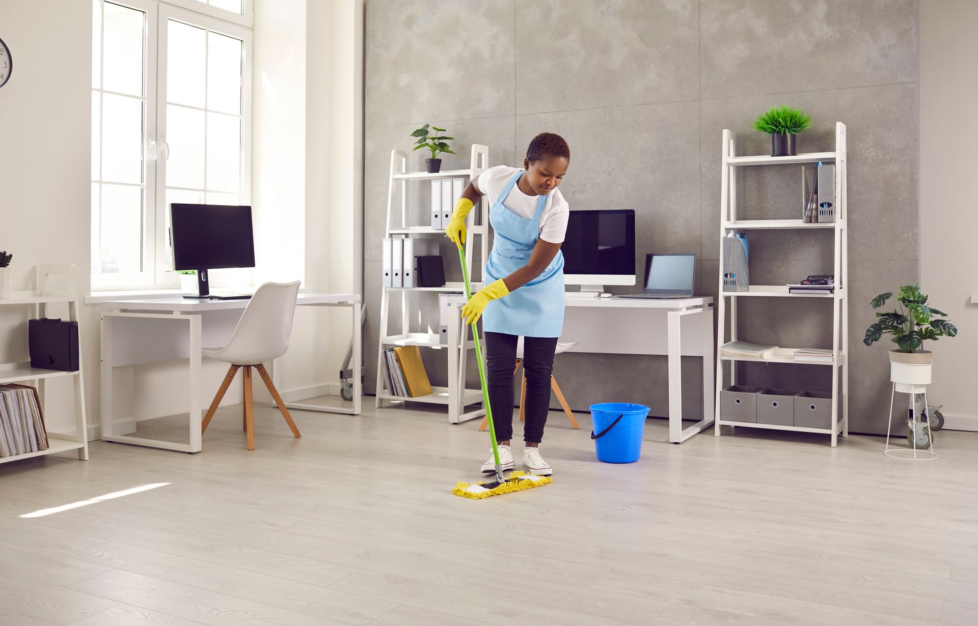 A female janitor with a mop cleans the office floor.