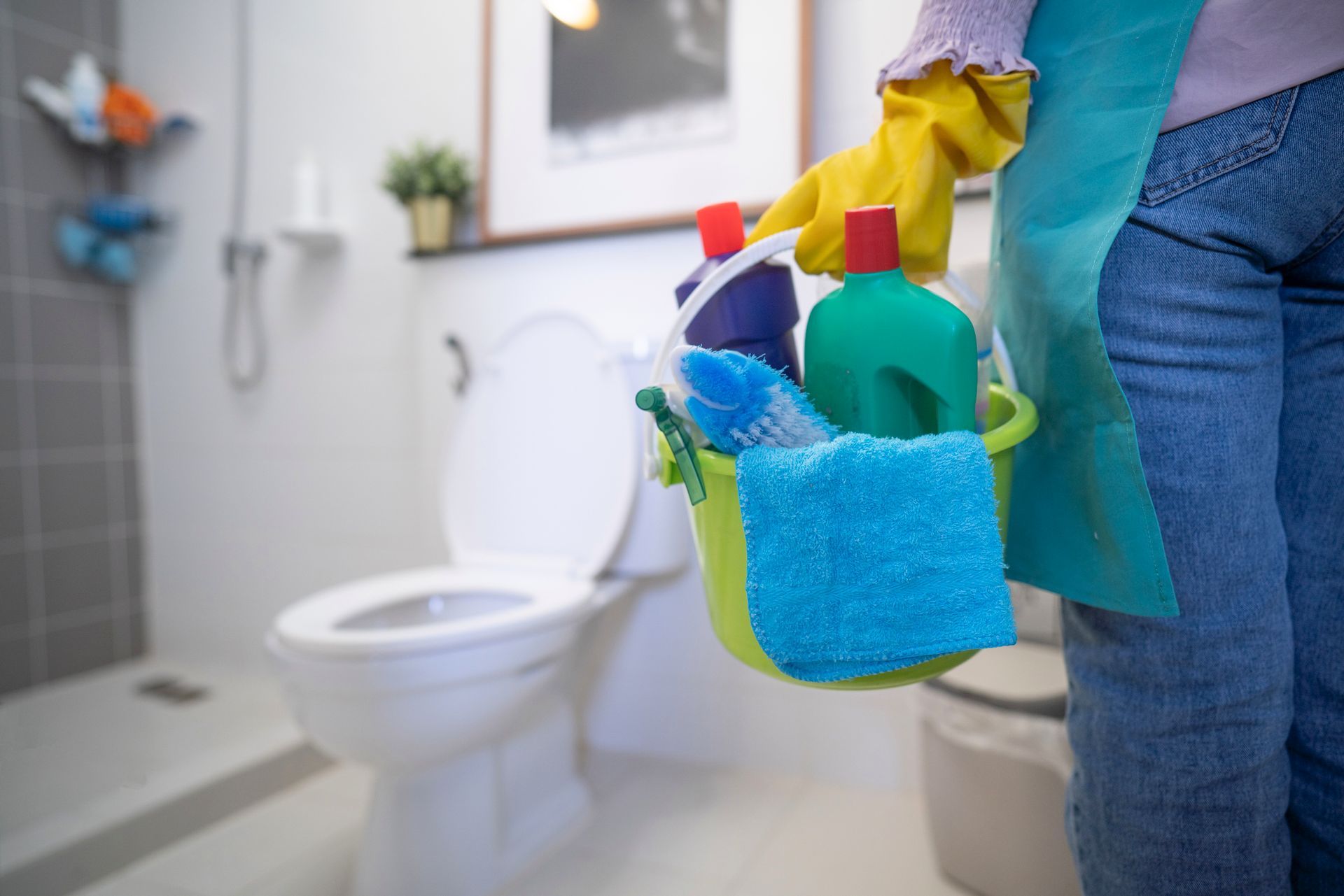Person holding a bucket of cleaning supplies in a modern bathroom setting. 