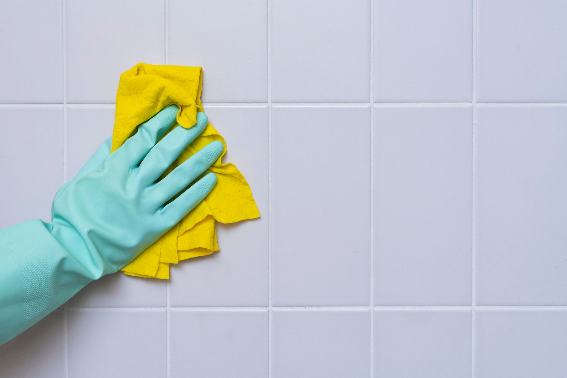 Gloved hand wiping white tiles with a yellow cloth during cleaning routine. 