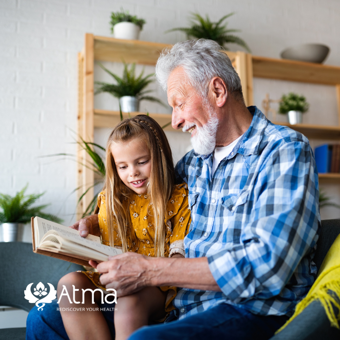 a man and a little girl are sitting on a couch reading a book .