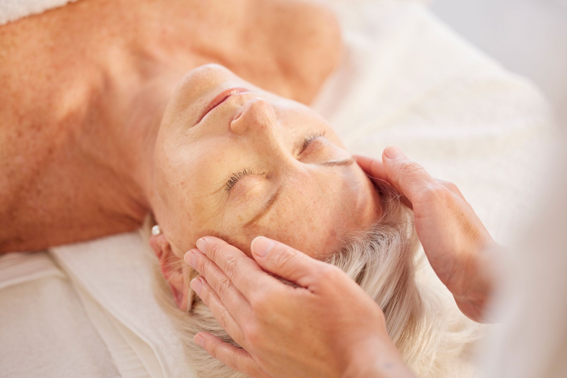 An older woman is getting a head massage at a spa.