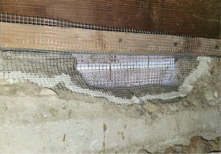 A wire mesh patch installed with mortar over a gap between a wooden sill plate and a concrete foundation wall.