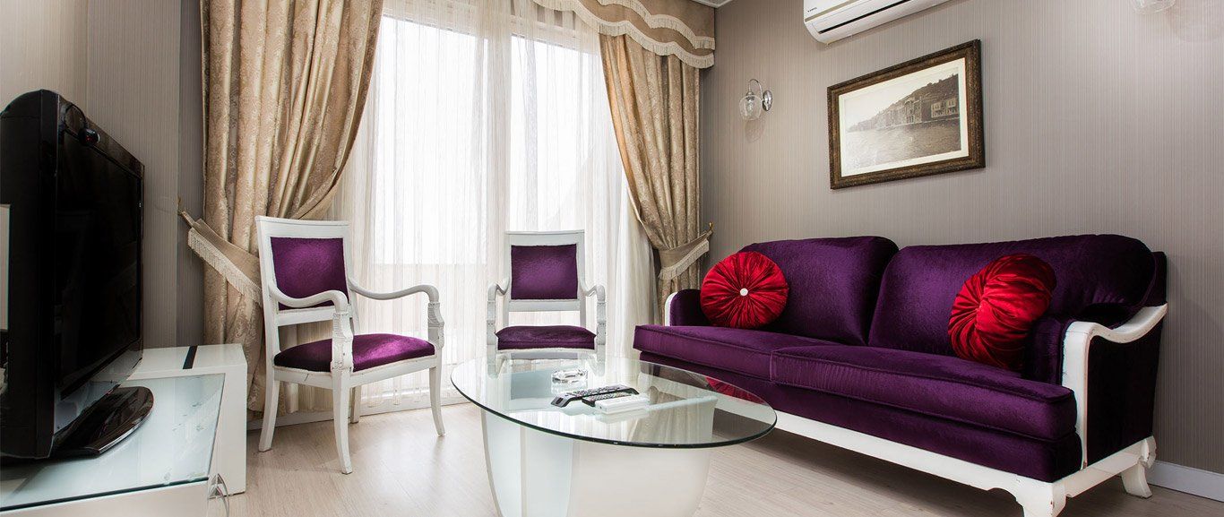 A living room with a purple couch , chairs , and a television.