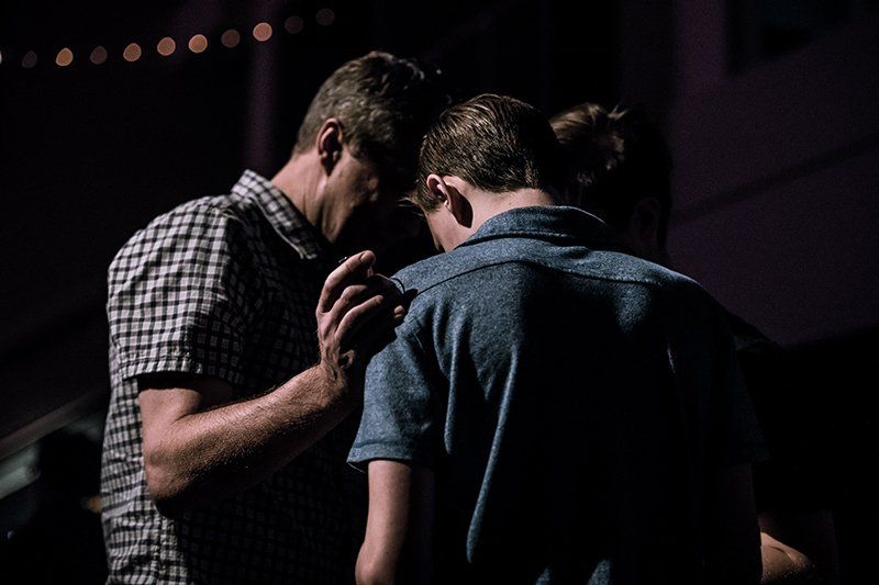 Two men are praying together in a dark room.