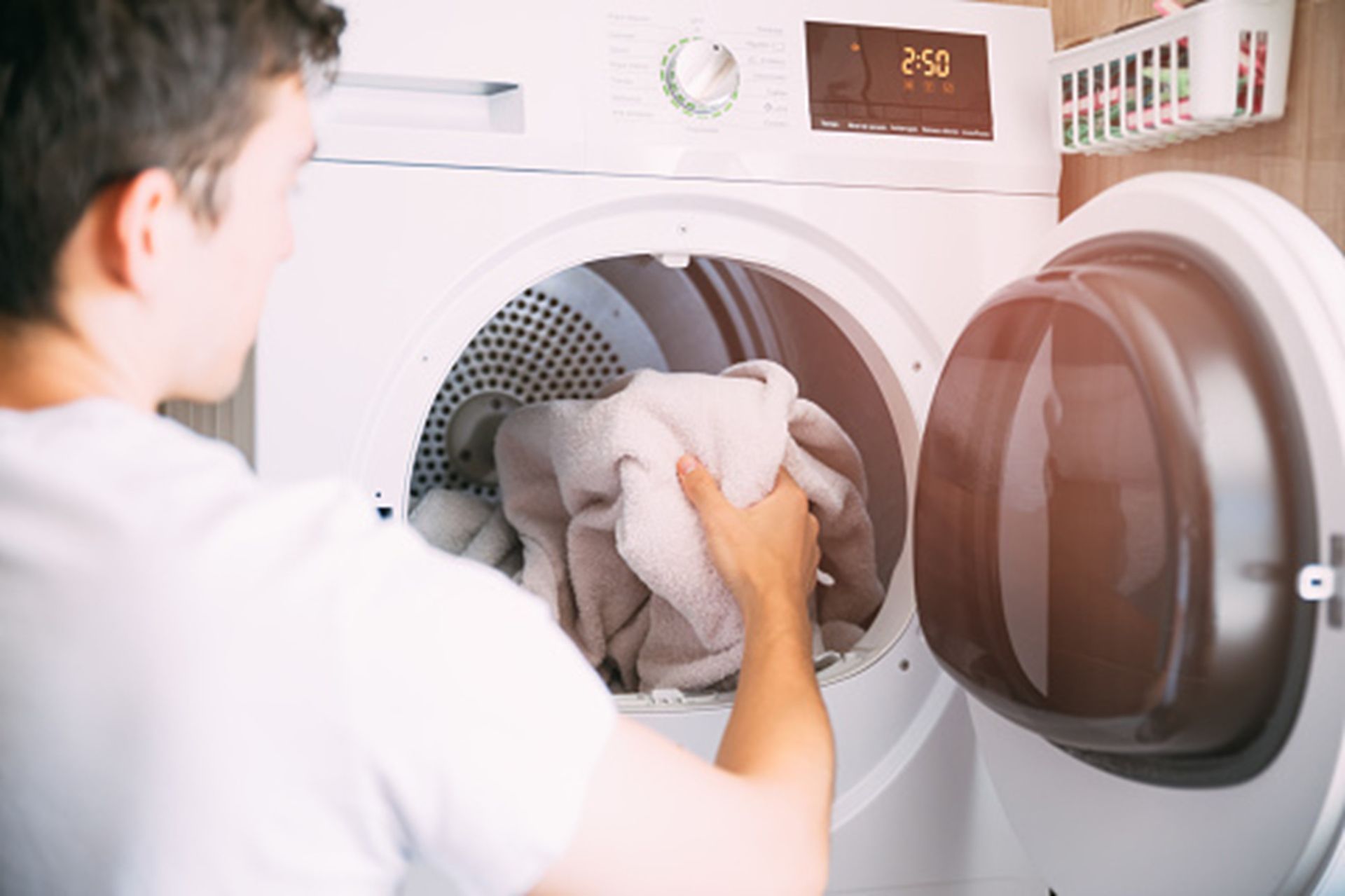 Close-up of a man wearing a white t-shirt, loading a second-hand dryer.