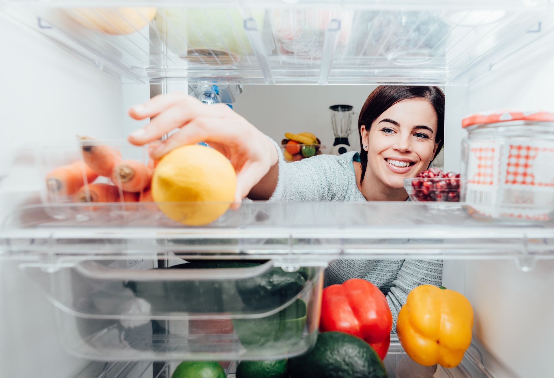 An inside view of a woman taking a lemon out of a fridge full of fresh produce.