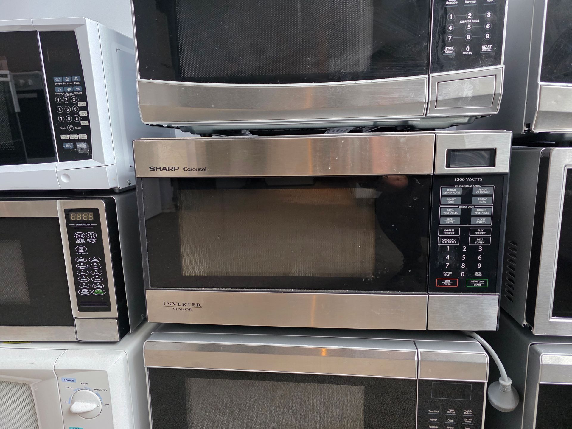 Microwaves stacked on top of each other, stainless steel front, various brands and sizes.