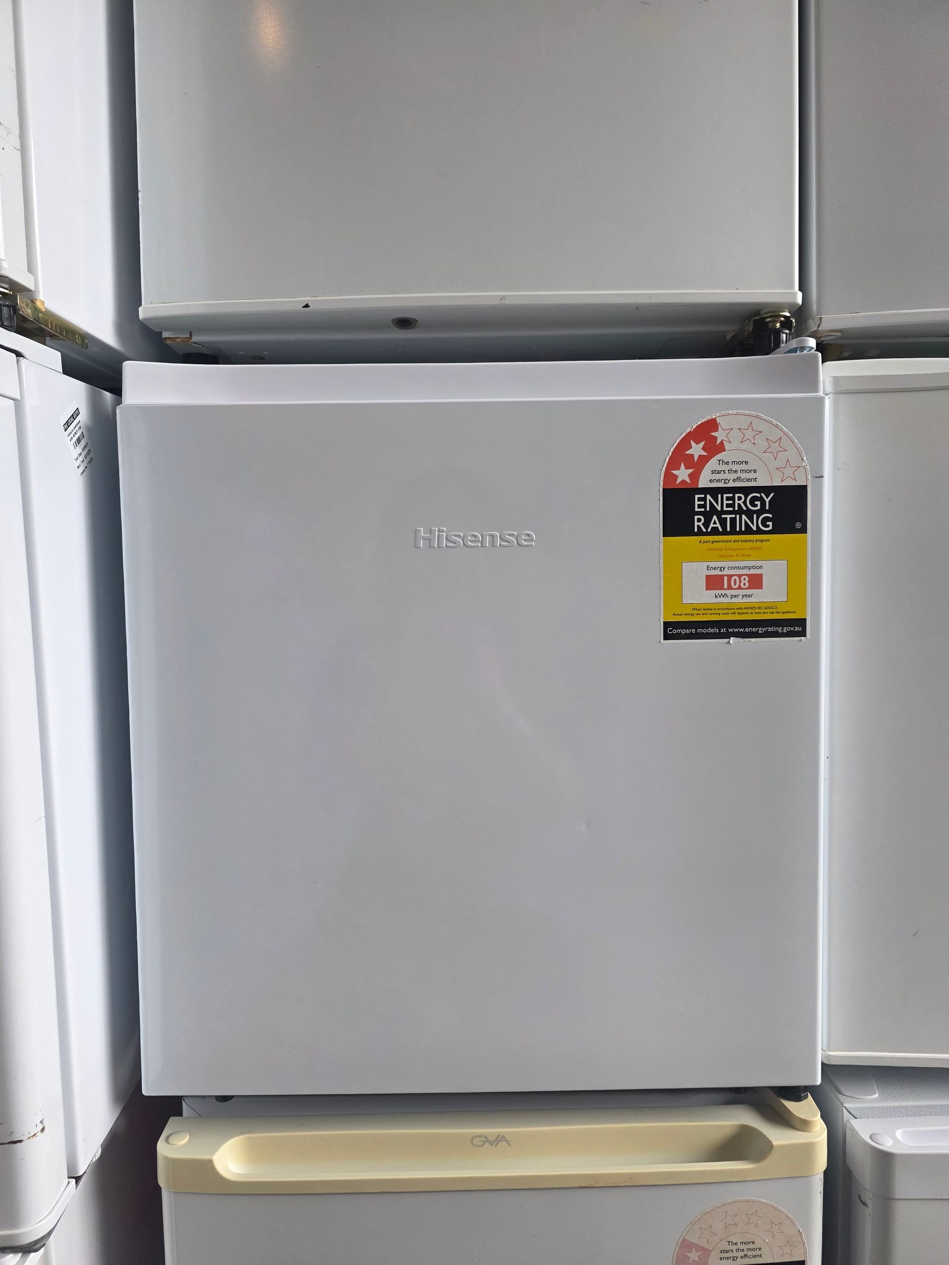 White mini-fridge with energy rating sticker, stacked amongst other appliances.