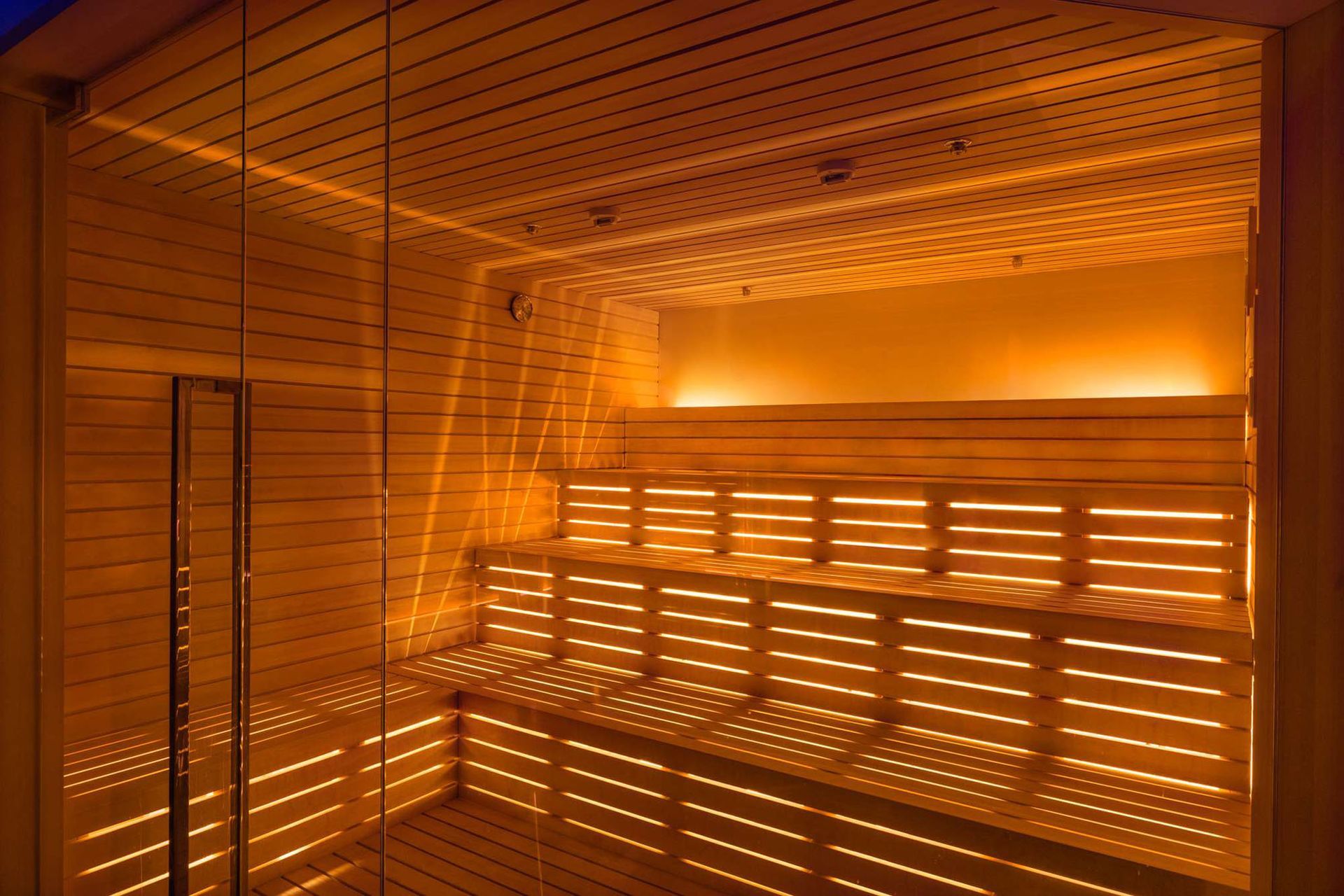 All'interno una sauna in legno con panche a più livelli, illuminata da luci calde.