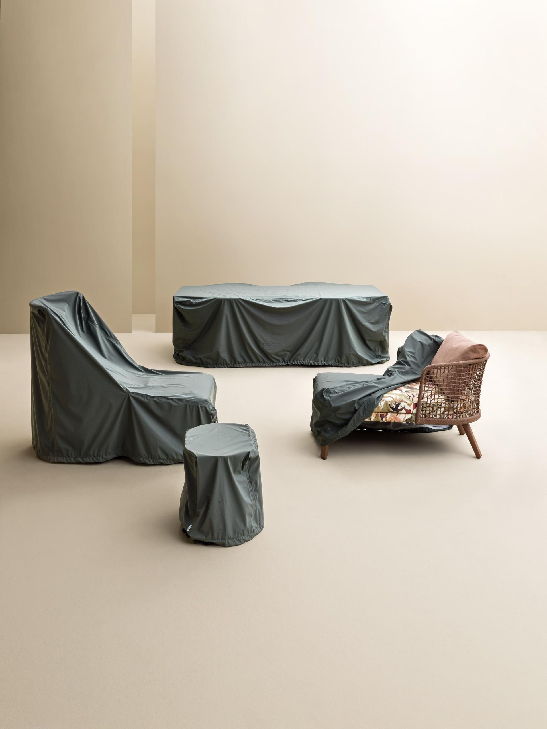 Quattro mobili da esterno coperti da teloni verde scuro; sfondo neutro.