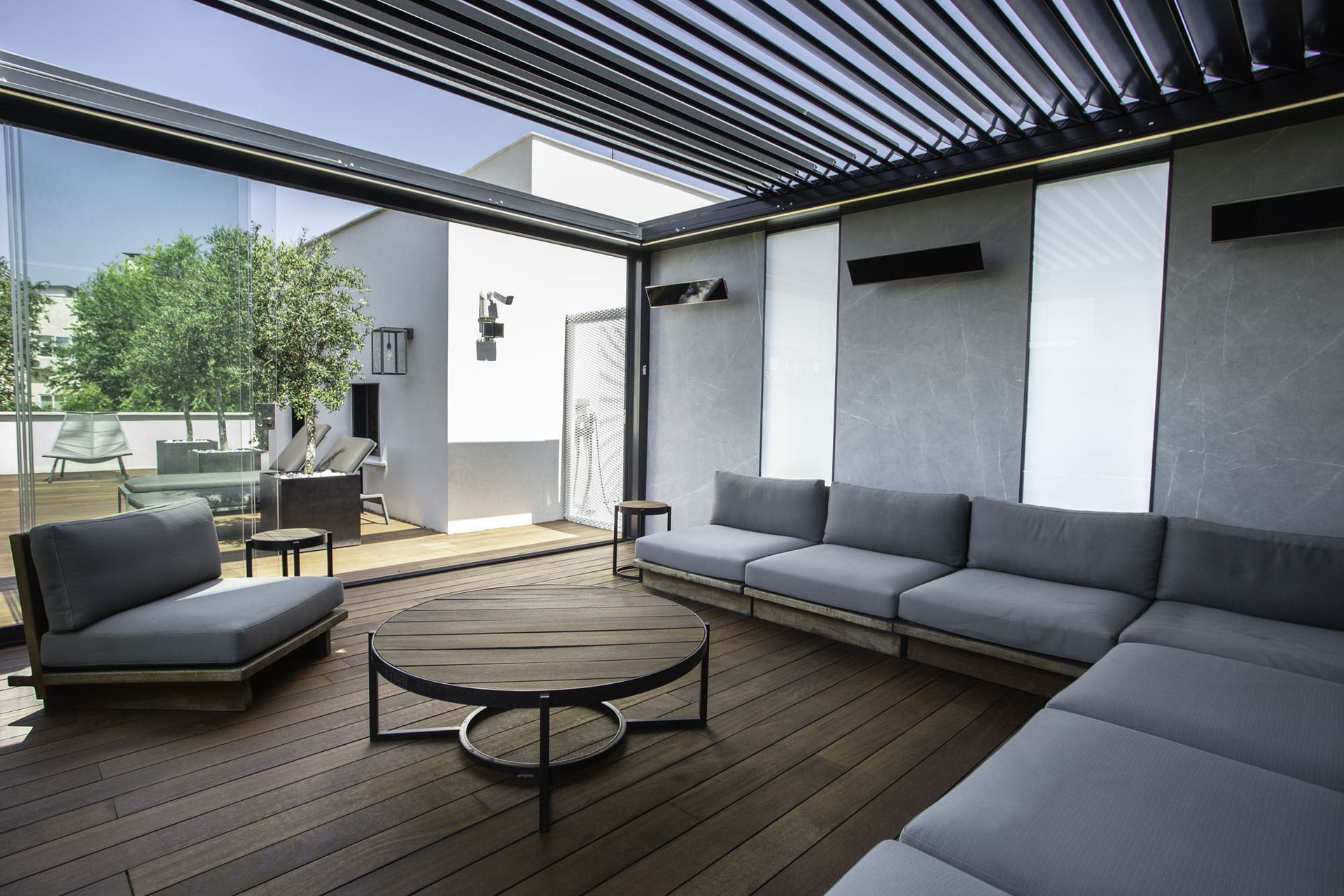 Moderno spazio abitativo all'aperto con divano componibile grigio, tavolino rotondo e tetto retrattile.