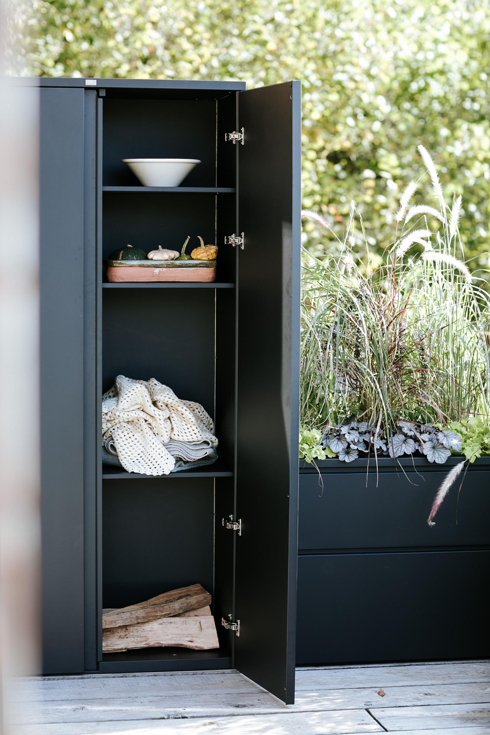Mobiletto portaoggetti da esterno grigio scuro con ante aperte, pieno di oggetti.