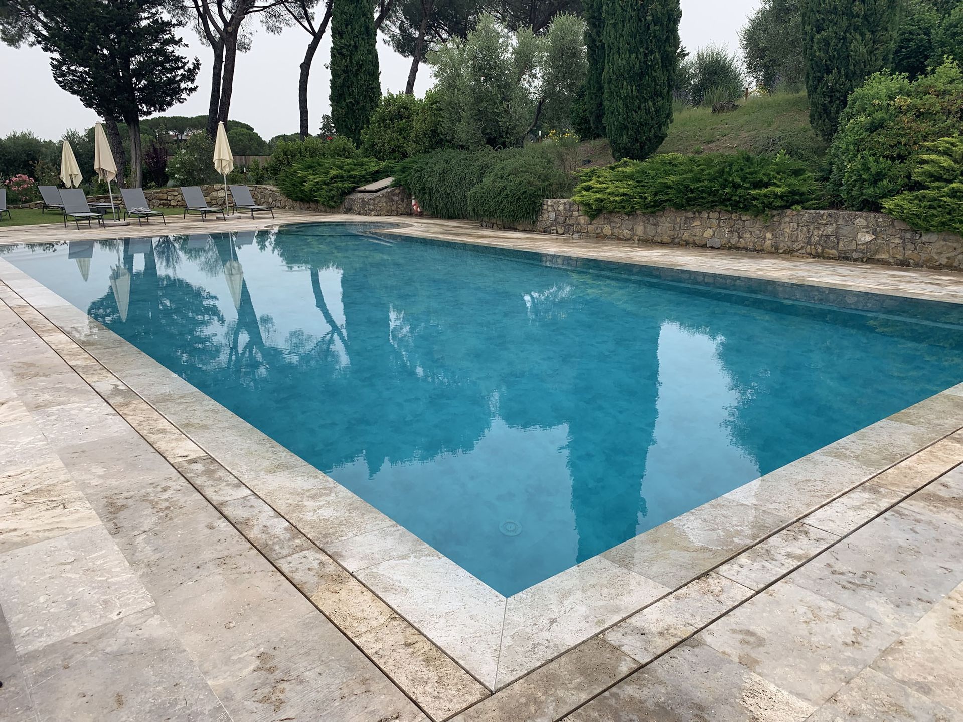 Piscina con acqua azzurra e pietra circostante, circondata da alberi e fogliame.
