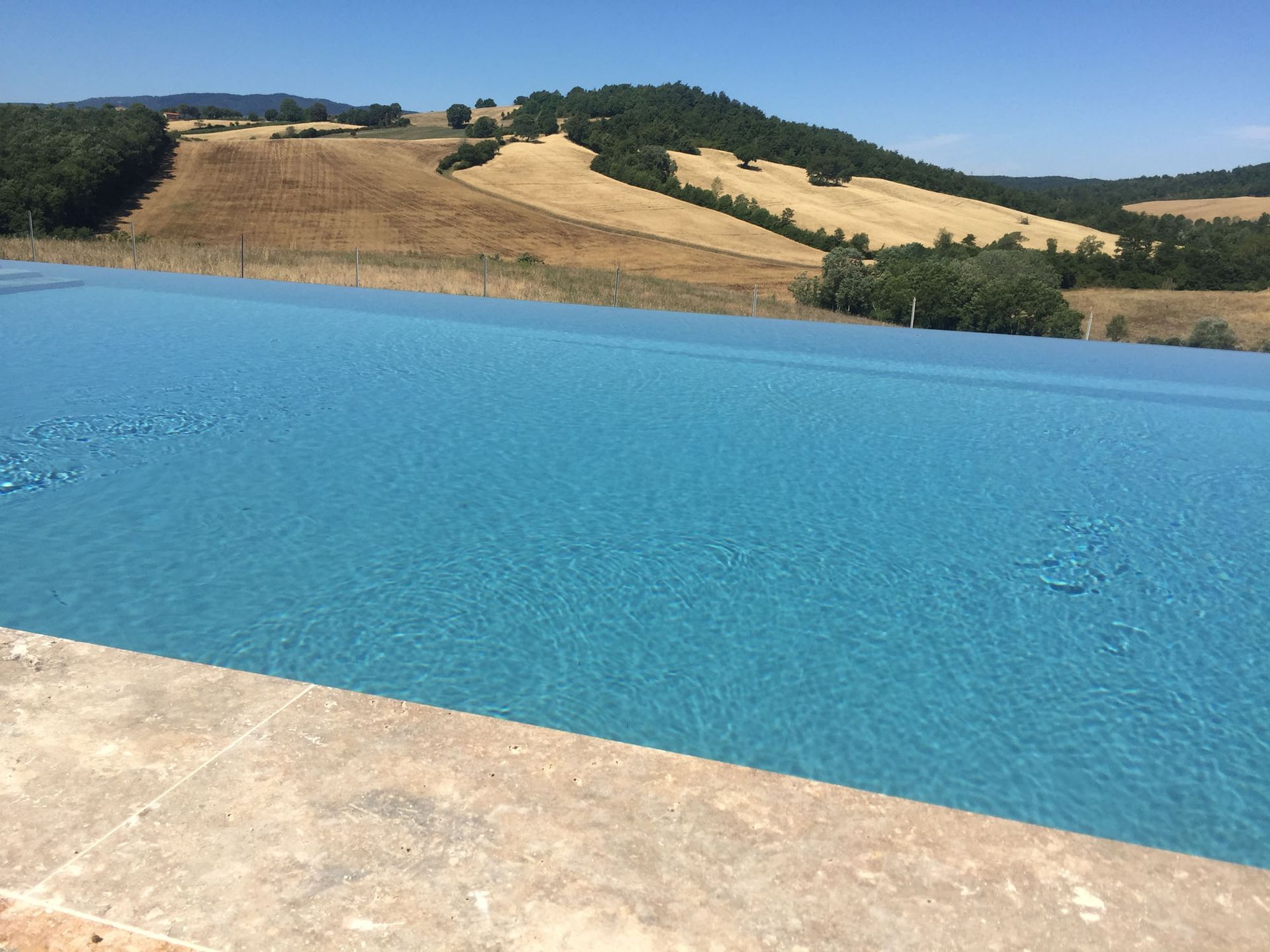 Piscina a sfioro con vista su un paesaggio arido ed erboso e su colline lontane sotto un cielo azzurro.