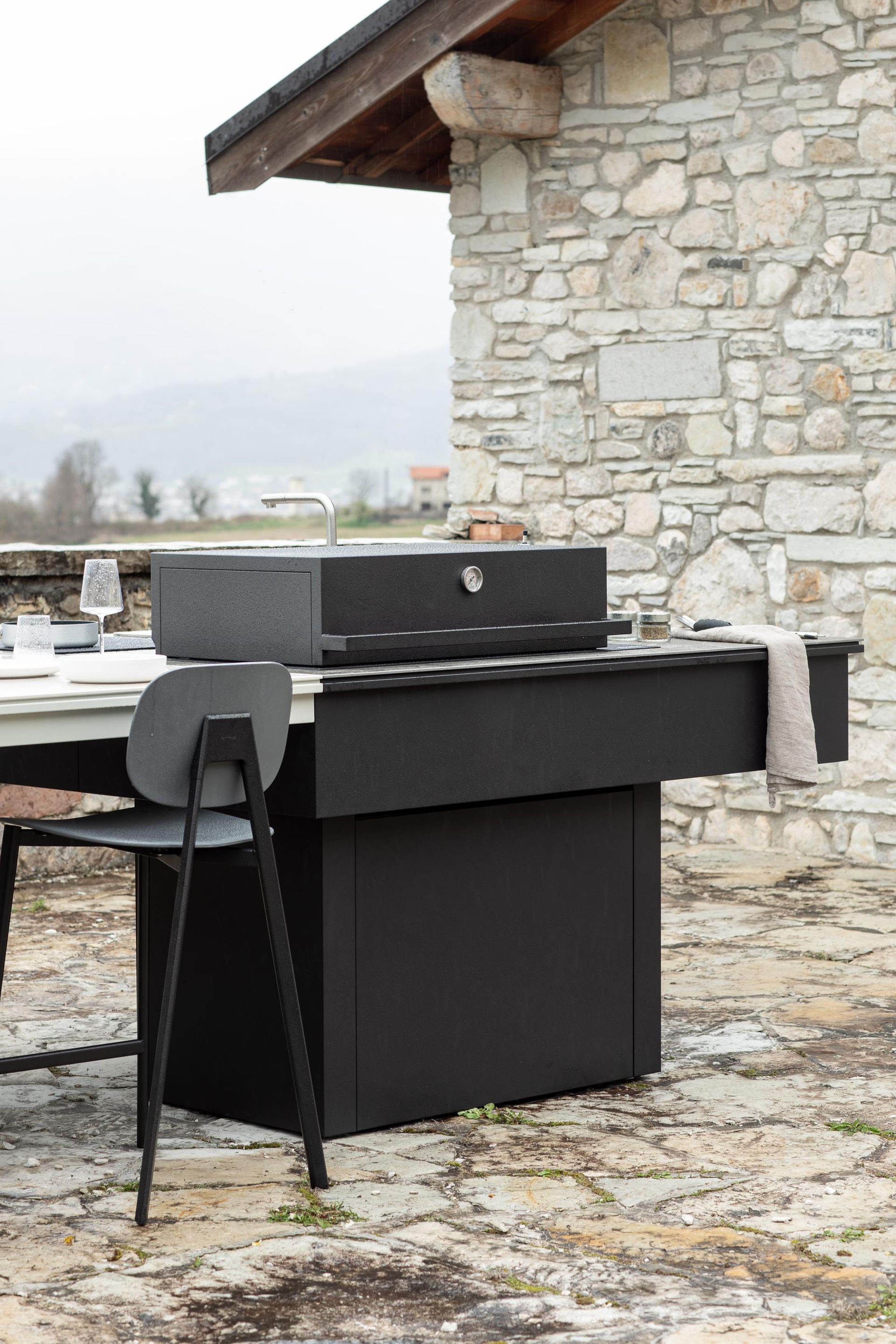 Griglia nera all'aperto su un patio, accanto a un tavolo e a un muro di pietra.