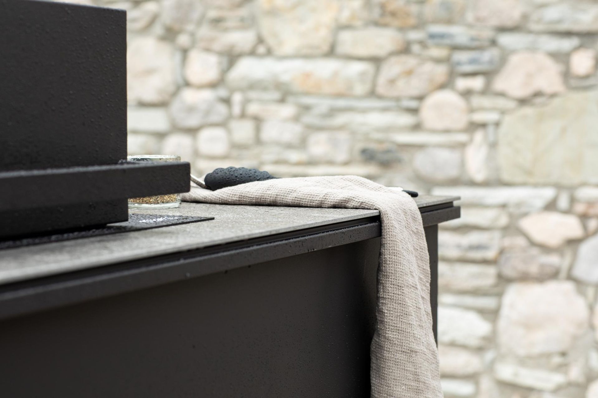 Stufa in metallo nero con asciugamano, sfondo muro in pietra.