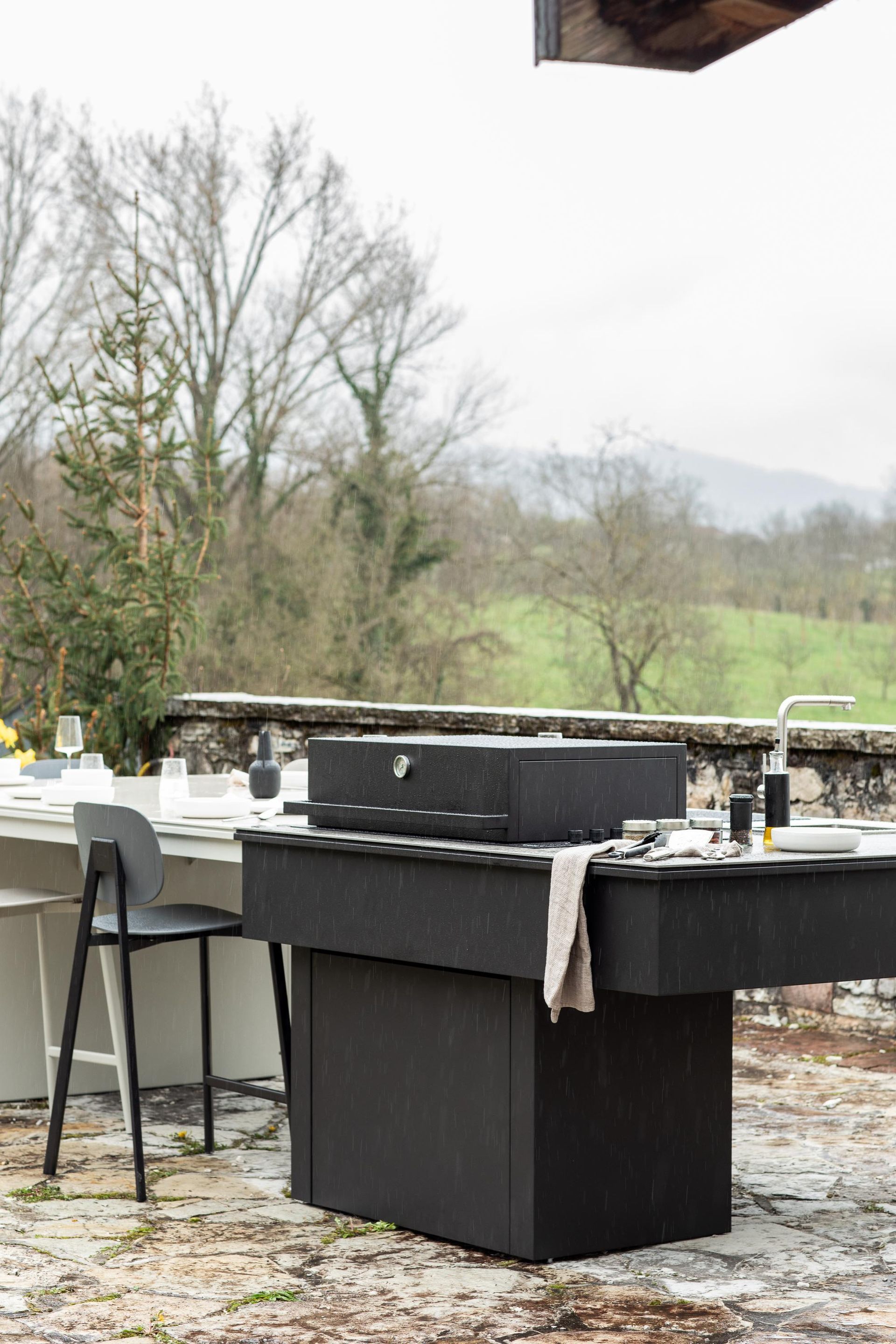 Isola cucina esterna con griglia nera e lavello, con vista su un suggestivo paesaggio verde.