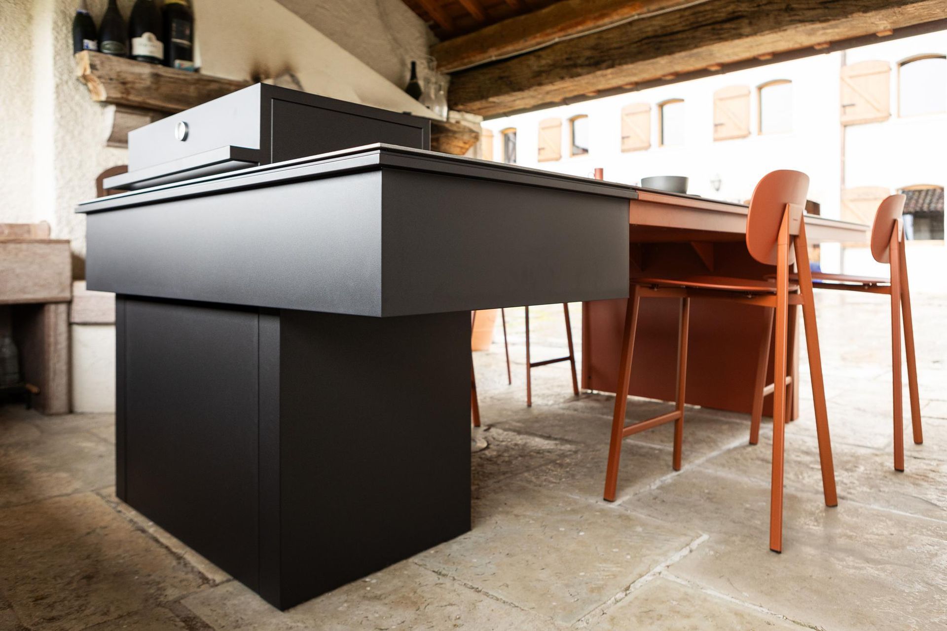 Isola da cucina nera per esterni con tavolo e sedie in un cortile in pietra.
