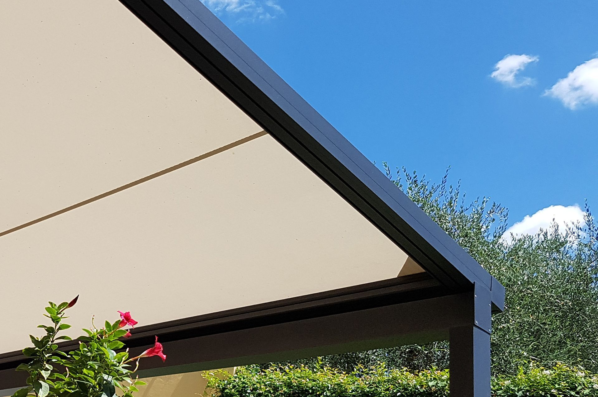 Tenda da sole retrattile beige su telaio nero, sullo sfondo di un cielo azzurro con un po' di verde.