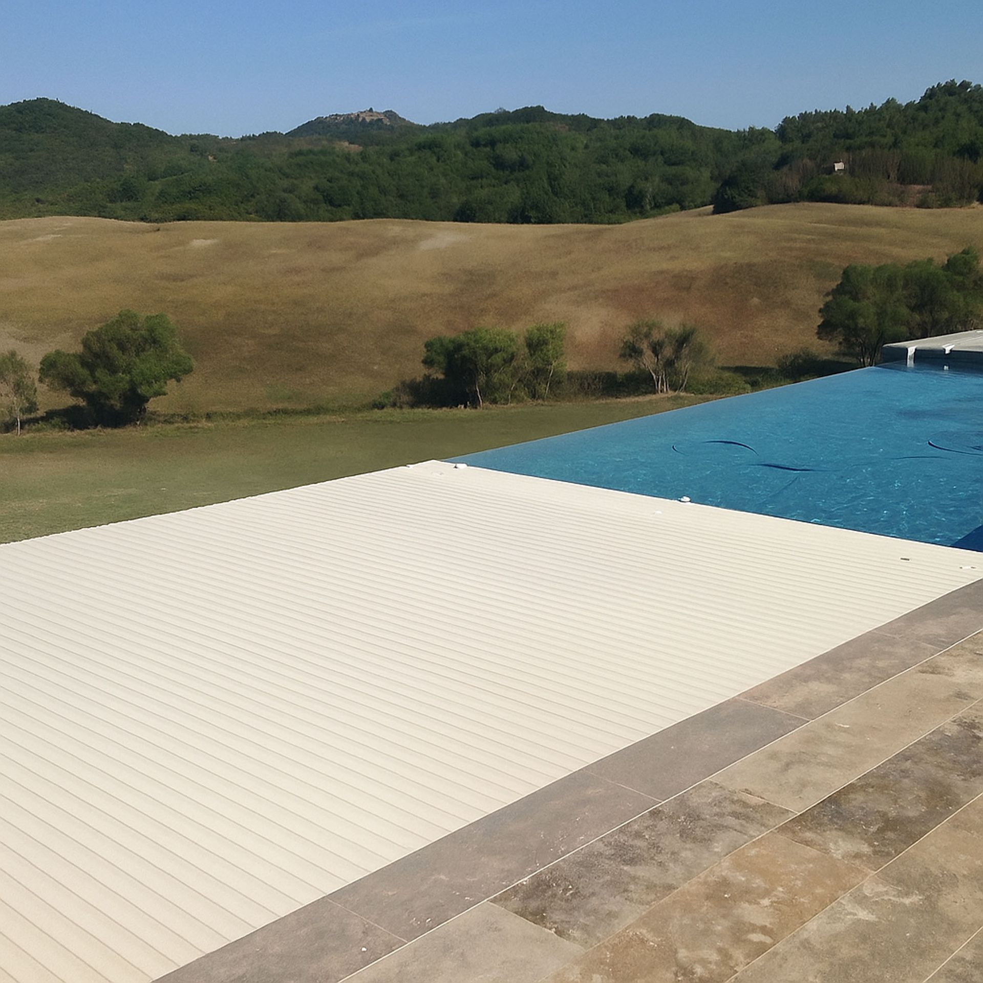 Piscina con copertura bianca chiusa, con vista su un campo erboso e sulle colline sotto un cielo soleggiato.