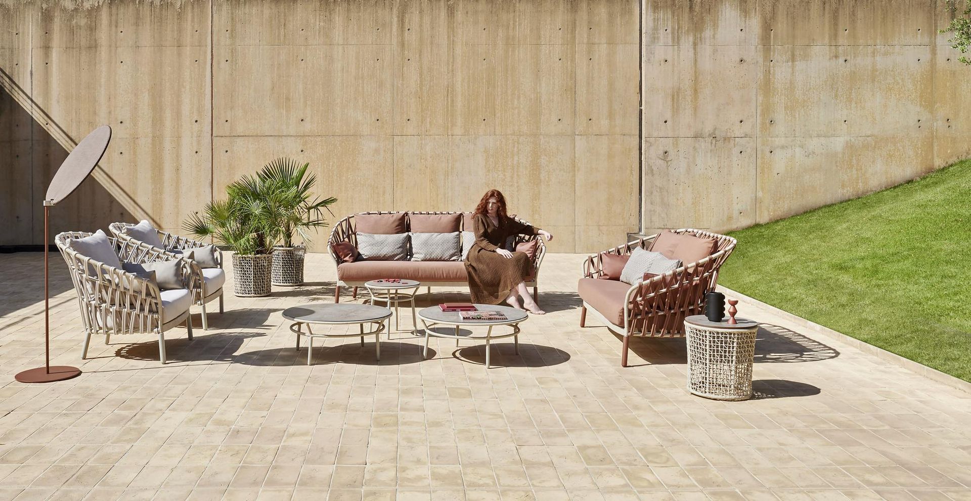 Set di mobili da esterno per patio con una persona, toni beige e rosa, sfondo con muro di cemento.