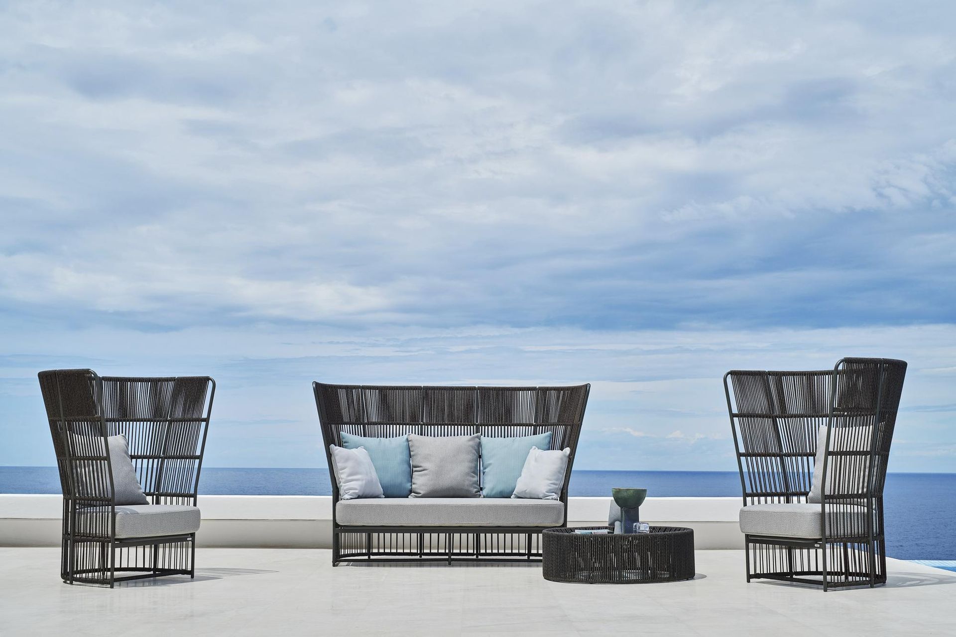 Arredi da esterno sistemati su una terrazza con vista sull'oceano, tra cui due sedie, un divanetto e un tavolino da caffè.