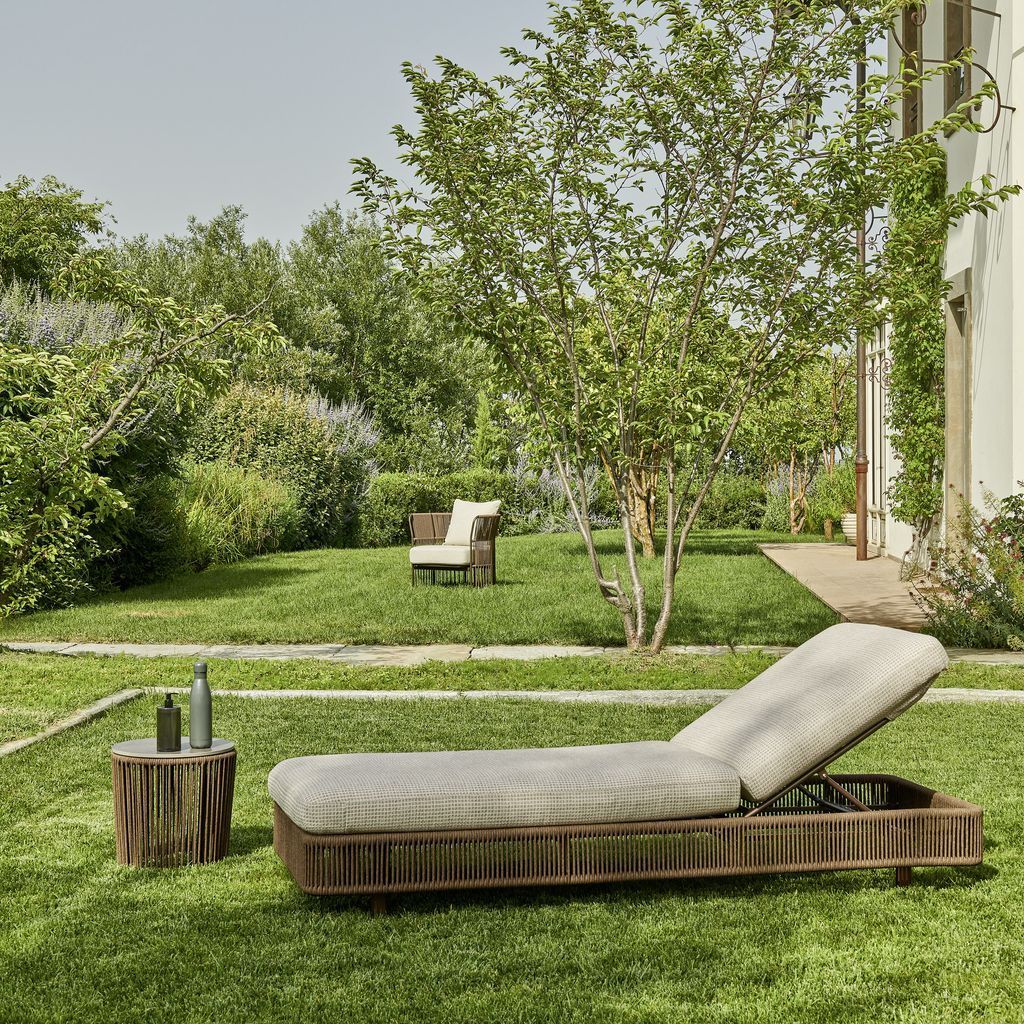Poltrona sul prato con tavolino, un'altra sedia sullo sfondo, alberi e un edificio in una giornata di sole.