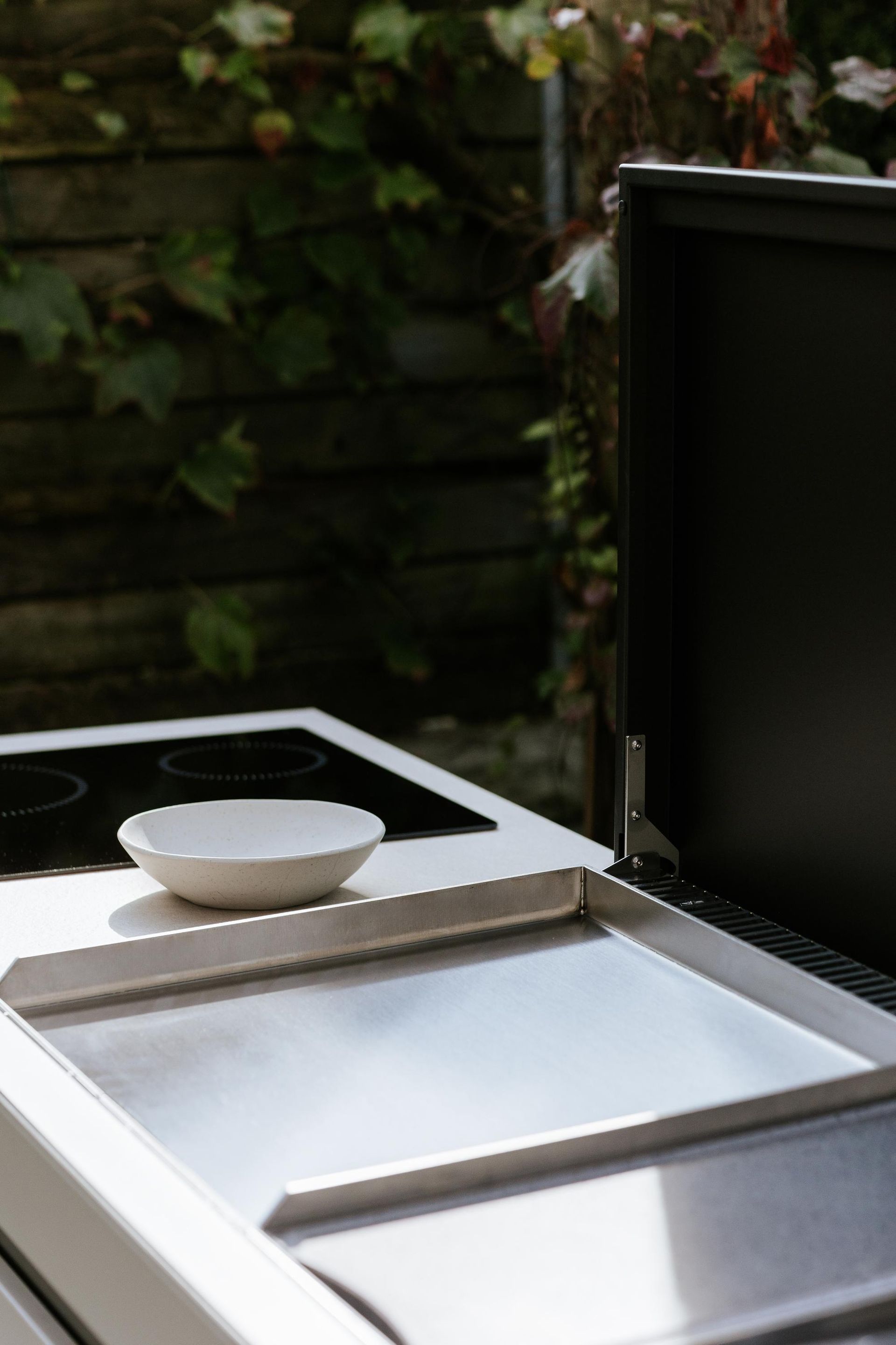 Cucina da esterno con piastra in acciaio inox e ciotola bianca su piano cottura nero.