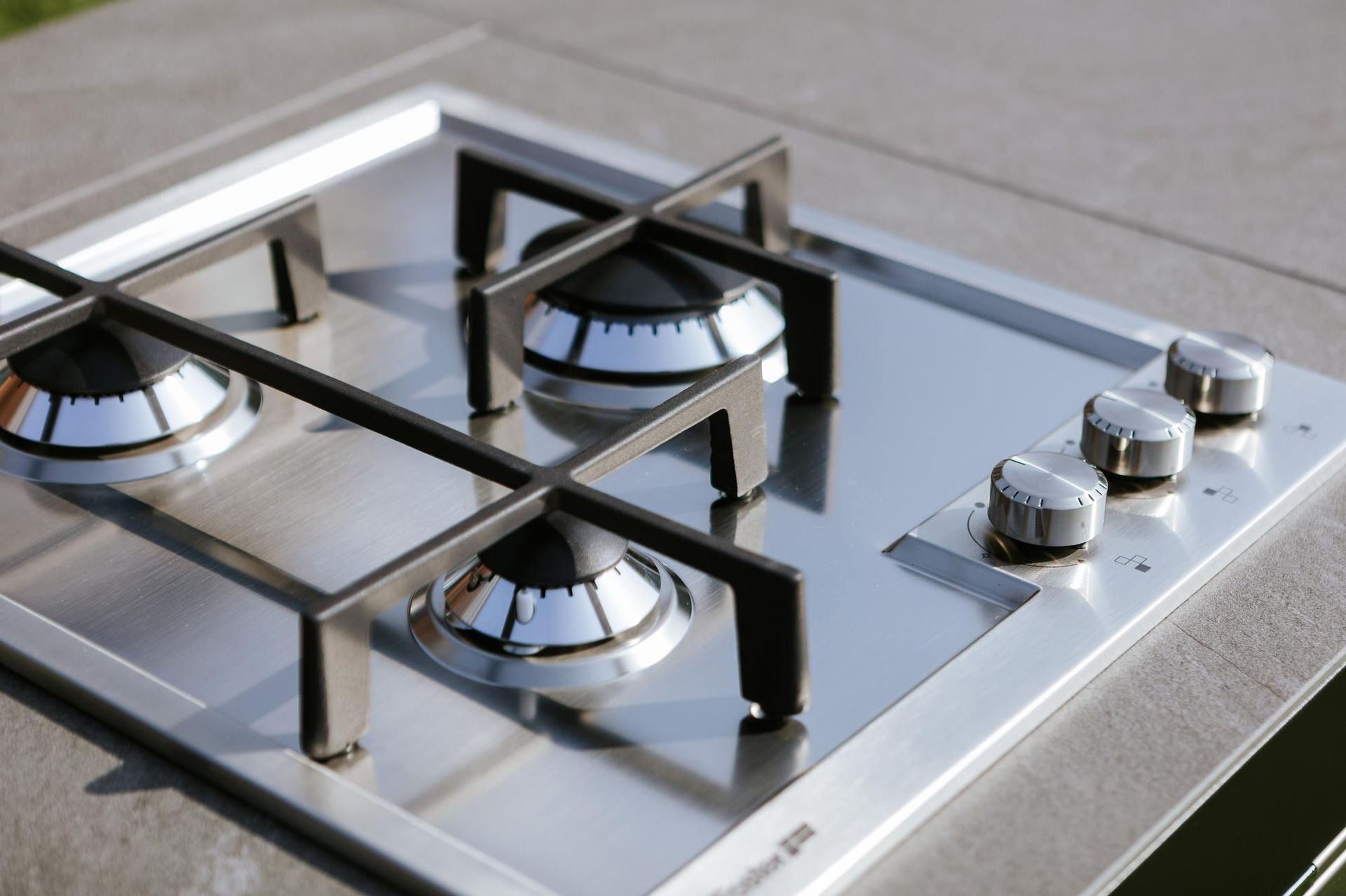 Piano cottura a gas in acciaio inox con quattro bruciatori, griglie nere e manopole di controllo argentate.