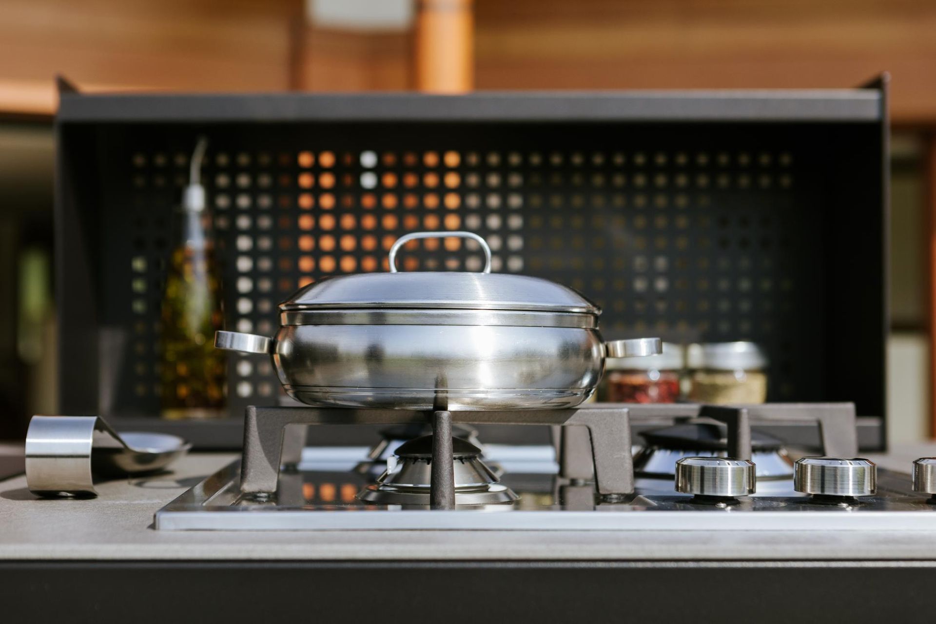 Pentola in acciaio inossidabile su un fornello a gas con paraschizzi nero e vari condimenti.