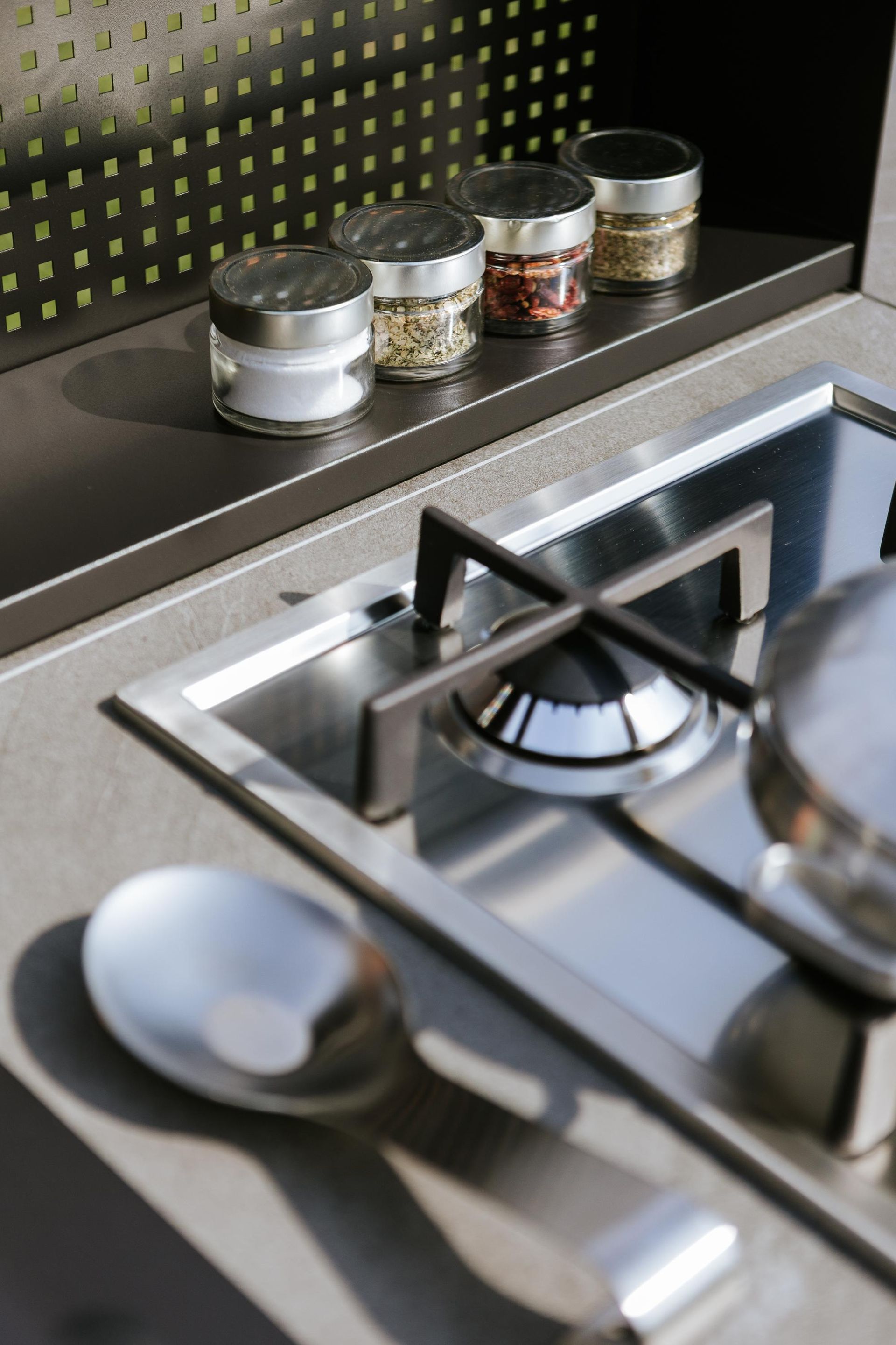 Primo piano di un piano cottura in acciaio inossidabile con barattoli di spezie su uno scaffale in una cucina all'aperto.