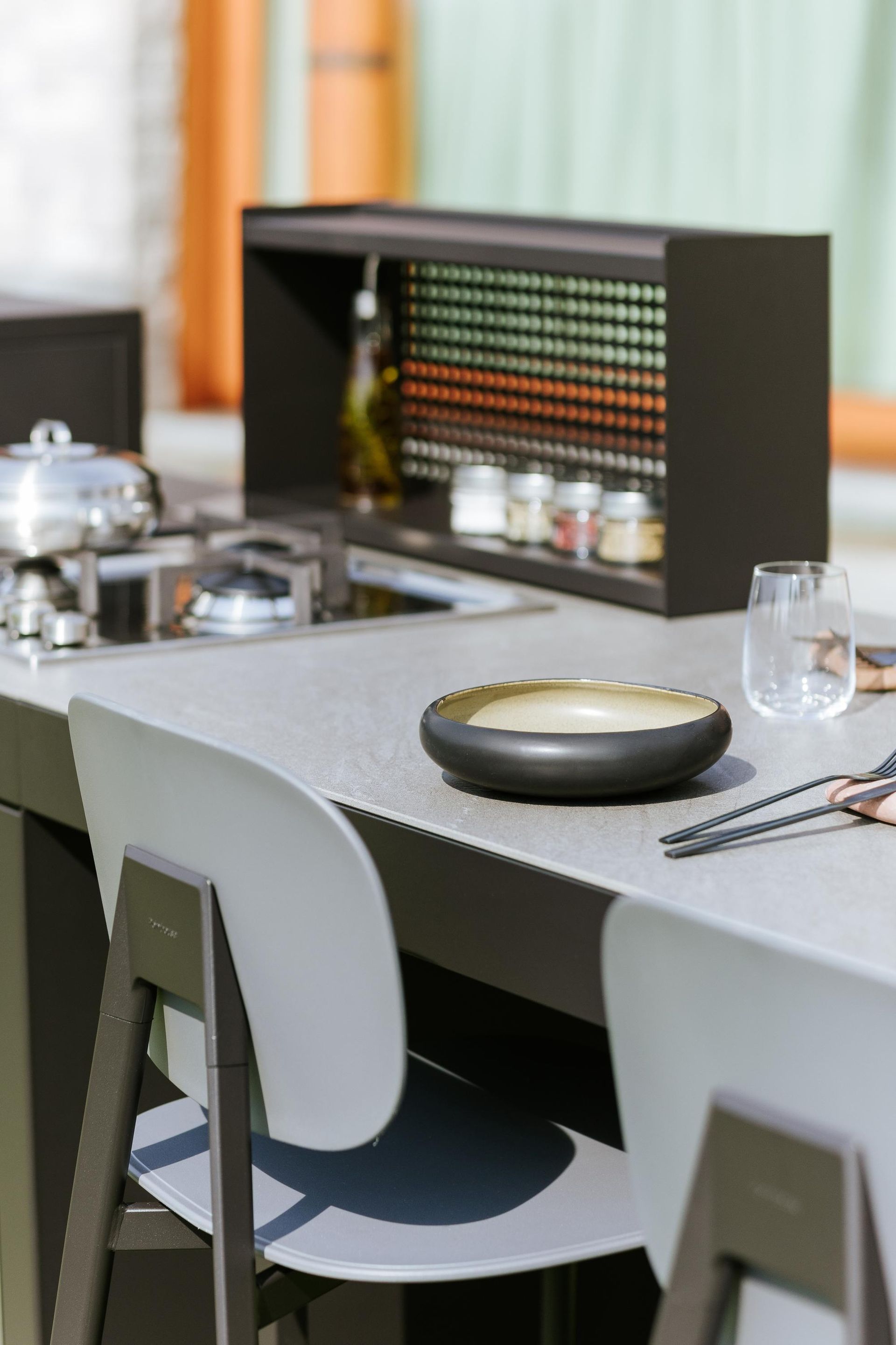 Bancone da cucina esterno con sgabelli, piano cottura, porta spezie e ciotola.