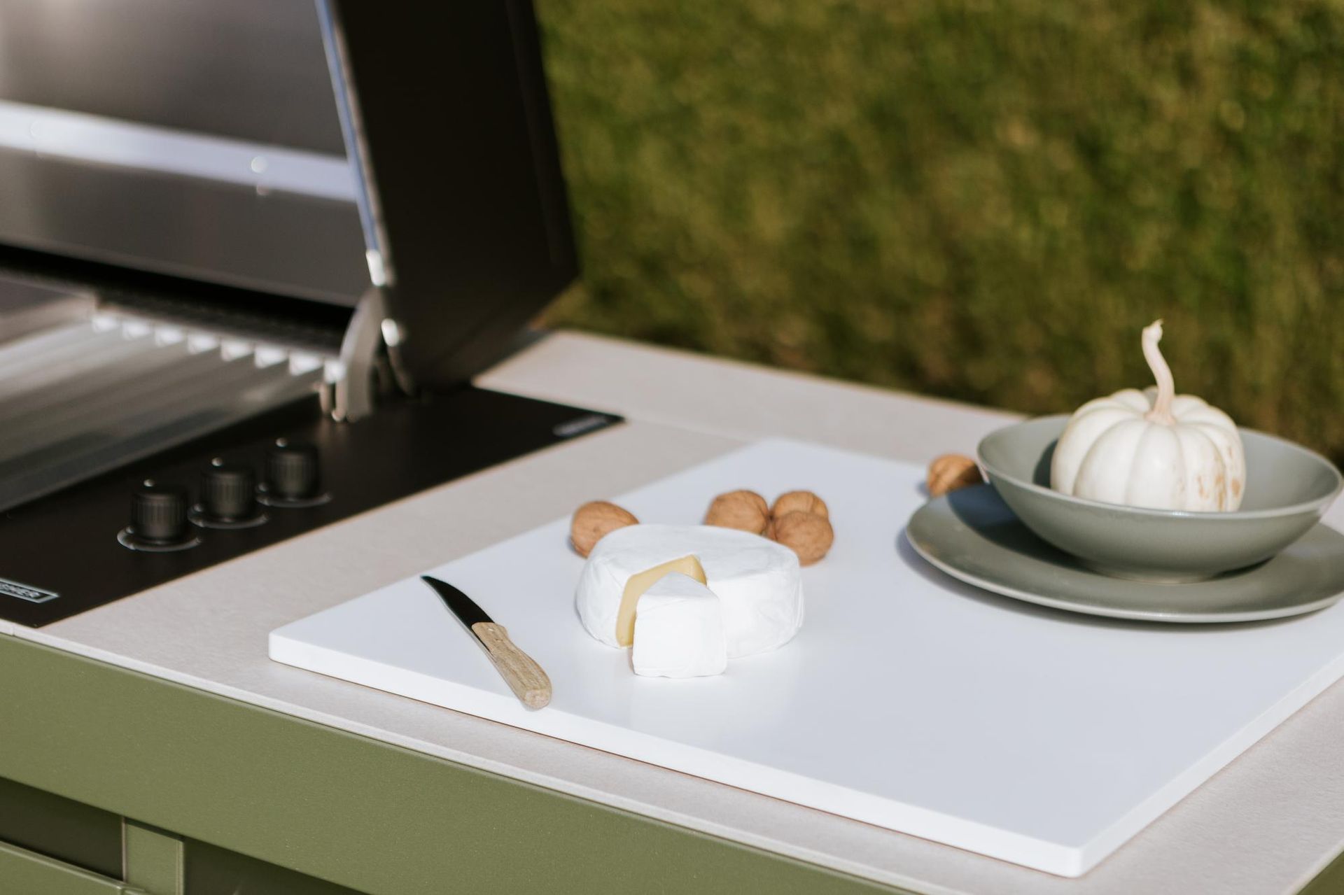 Formaggio bianco, uova e una zucca sono disposti su un tagliere bianco accanto a una griglia.