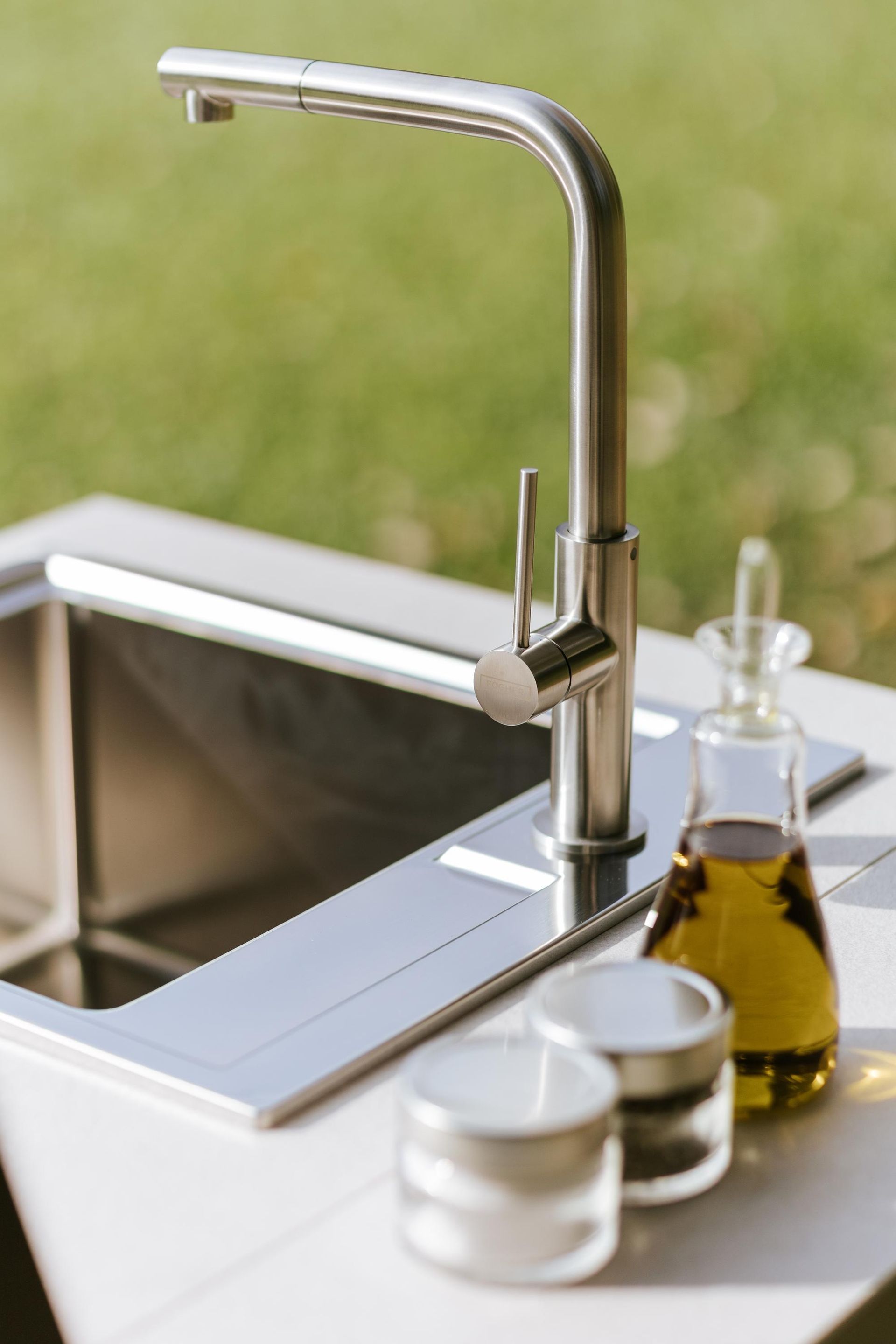 Lavello da cucina in acciaio inossidabile con rubinetto, barattoli e bottiglia di olio d'oliva, all'aperto.