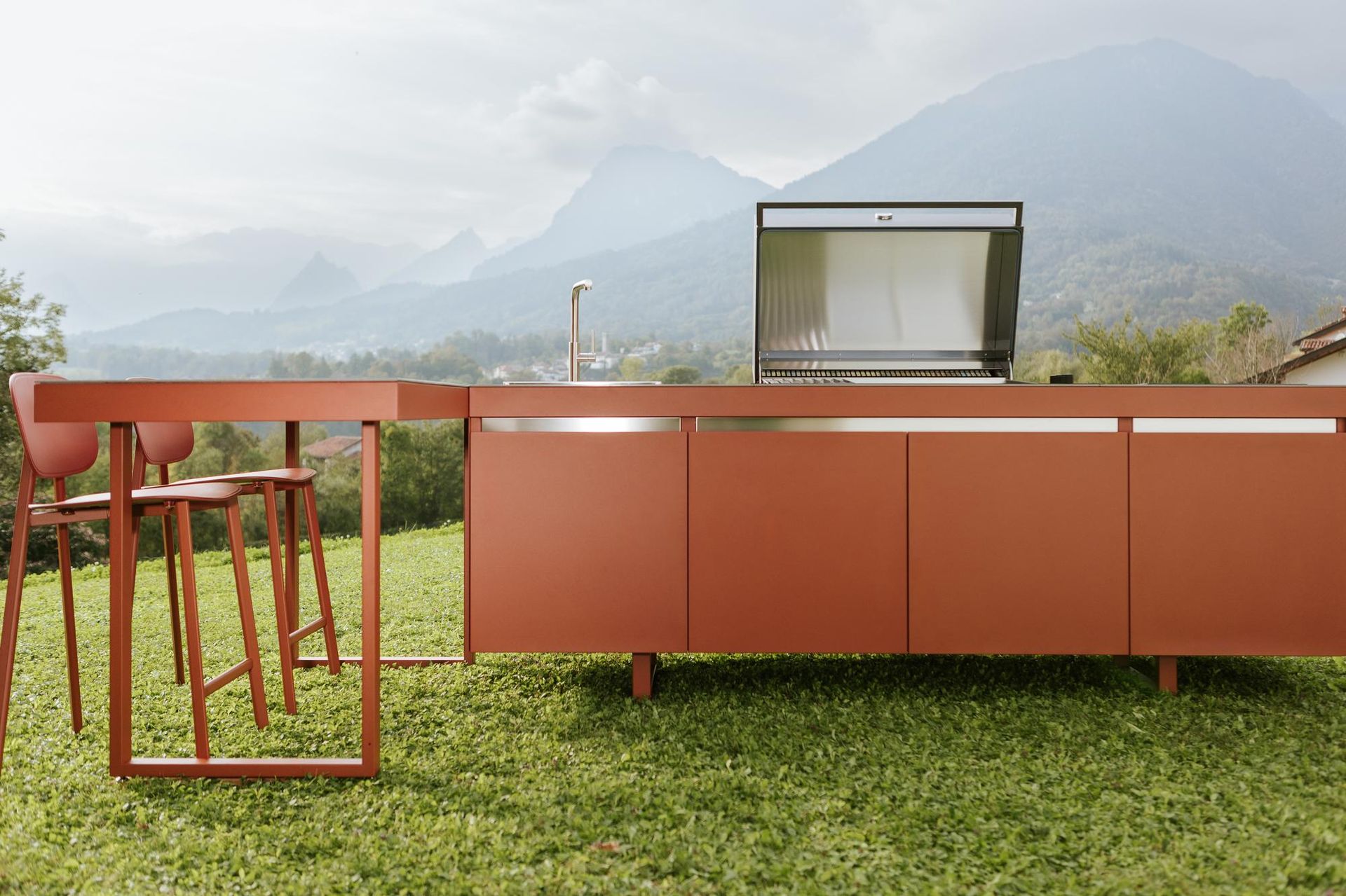 Cucina esterna con mobile color rame, griglia e sgabelli da bar, il tutto sullo sfondo di montagne.