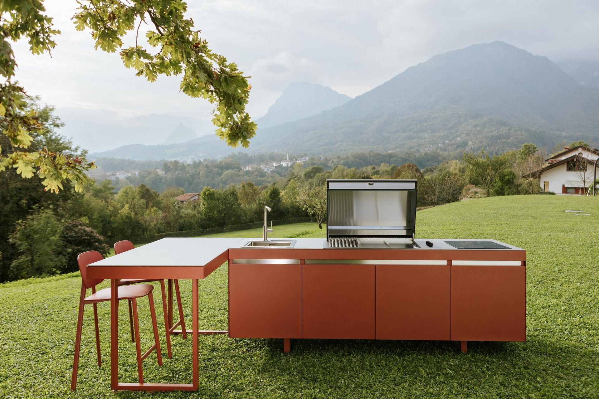 Cucina all'aperto con mobili color ruggine, tavolo e sedie su una collina erbosa, con le montagne sullo sfondo.