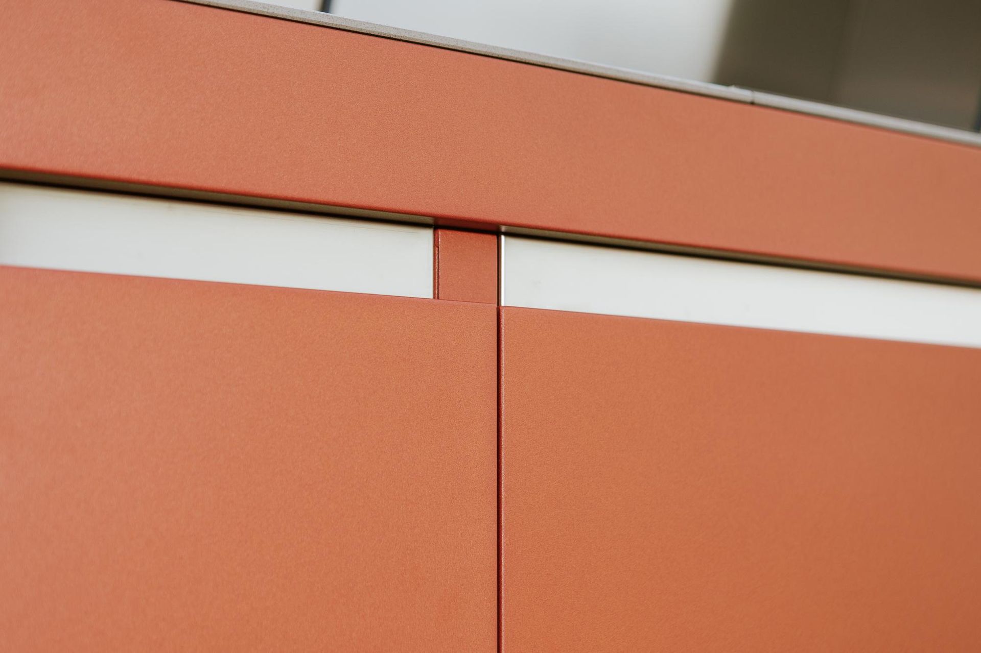 Primo piano delle ante dei mobili color terracotta con finiture bianche, unite da una linea verticale.