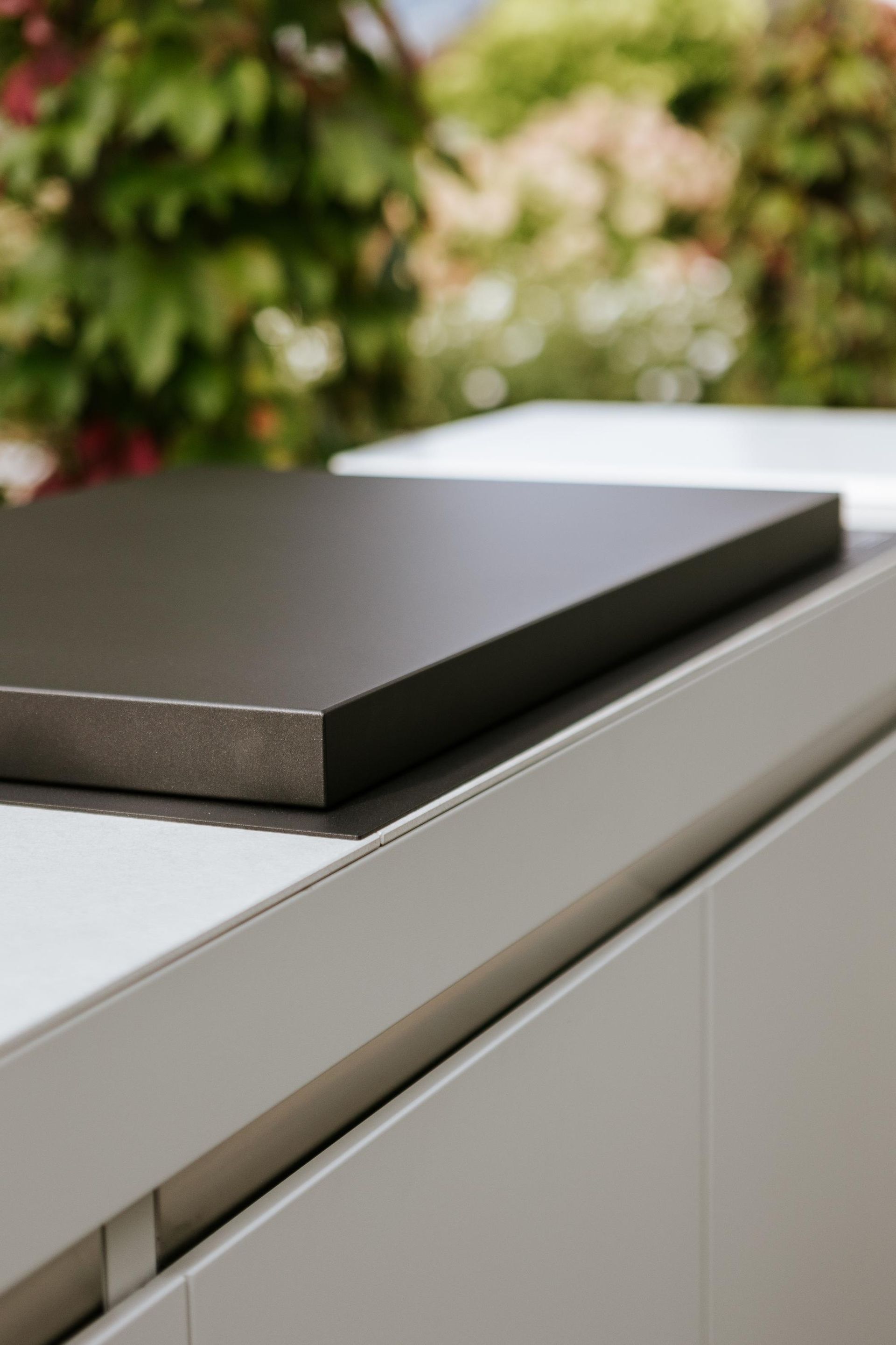 Primo piano di un piano di lavoro marrone scuro sopra un mobile bianco e grigio chiaro con uno sfondo verde sfocato.