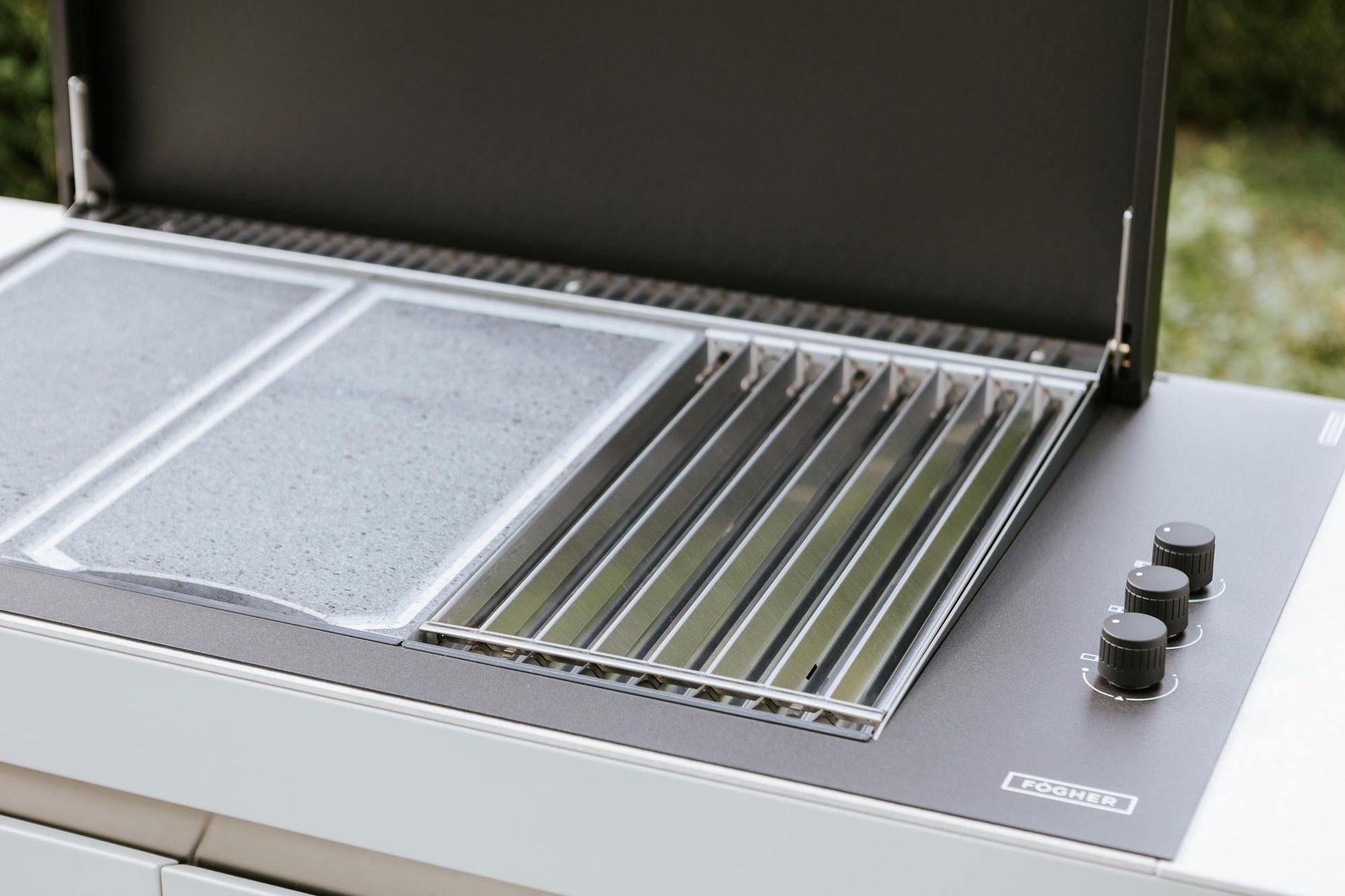 Barbecue da esterno con coperchio aperto, che mostra le griglie di cottura e le manopole di controllo.